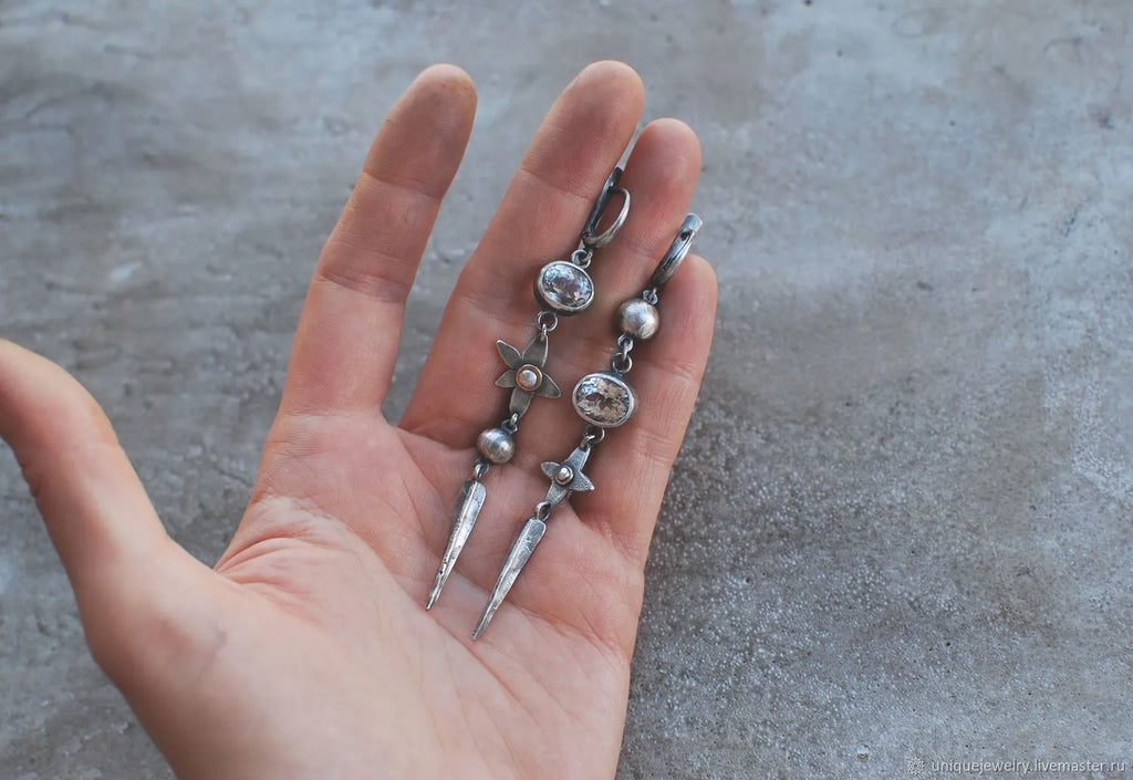 Pair of long geometric pendant earrings in antique silver with rhinestone detail on a white background.