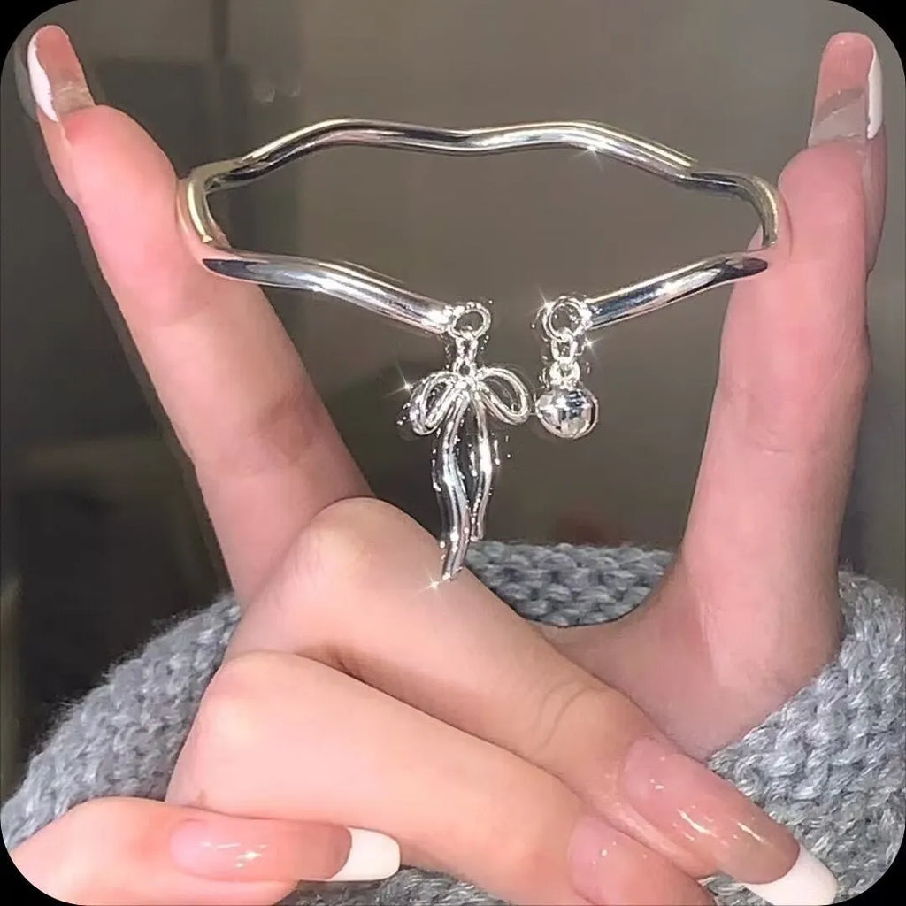 Silver adjustable bracelet with a detailed bow charm and bell opening.