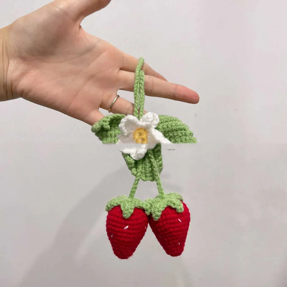 Handwoven strawberry-shaped car pendant made from cotton and hemp fibres on a grey background.