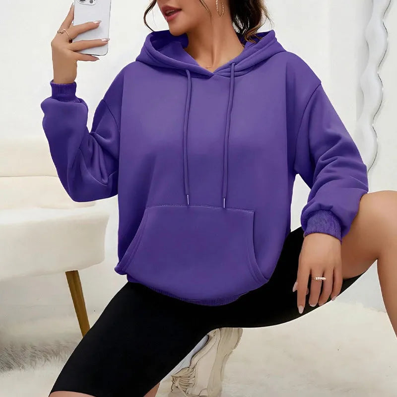 Woman wearing a loose grey drawstring hoodie with front kangaroo pocket, long sleeves.