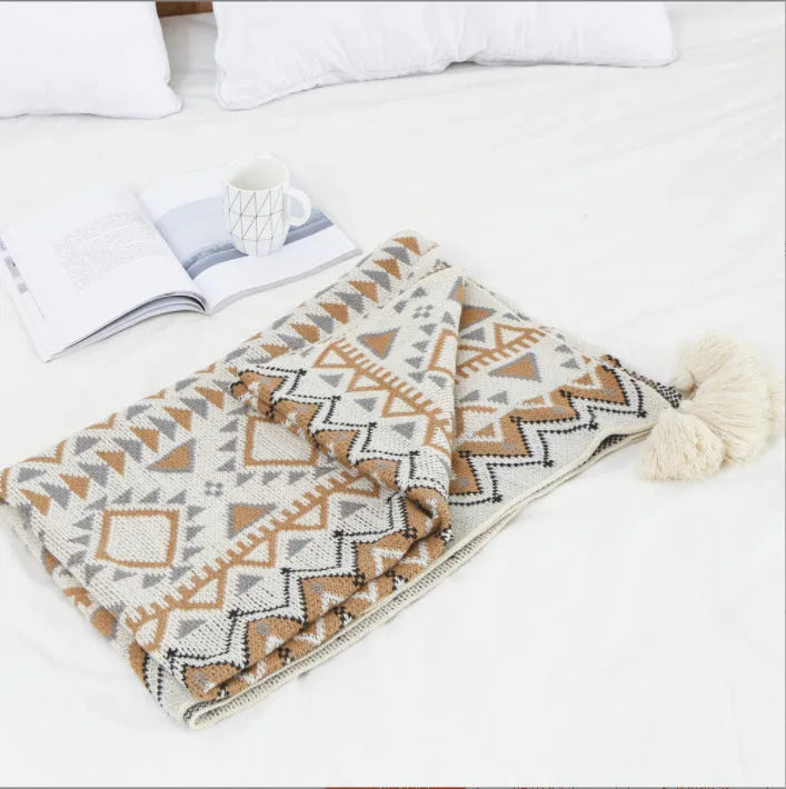 Large beige acrylic sofa blanket with tassel fringe draped over a grey sofa