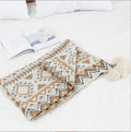 Large beige acrylic sofa blanket with tassel fringe draped over a grey sofa