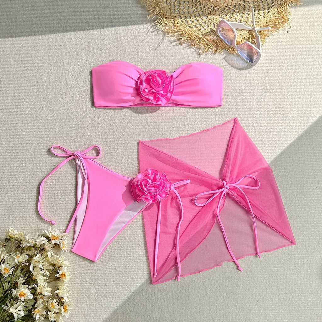 Women's pink tube top swimsuit with a large 3D flower tie, matching pants, and a skirt laid flat.