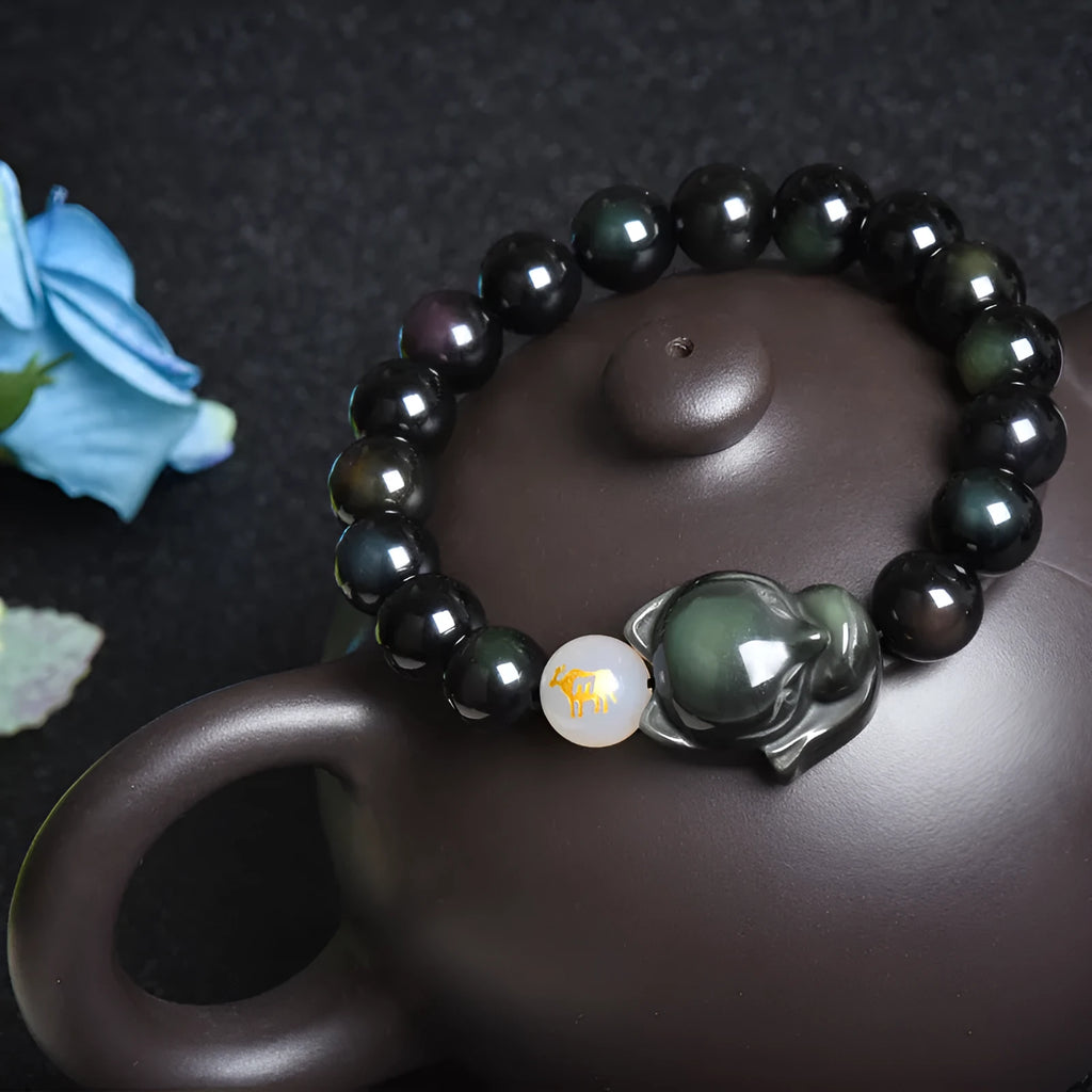 Natural black obsidian bracelet with 10mm beads on wrist, showing gold tone fastening option.