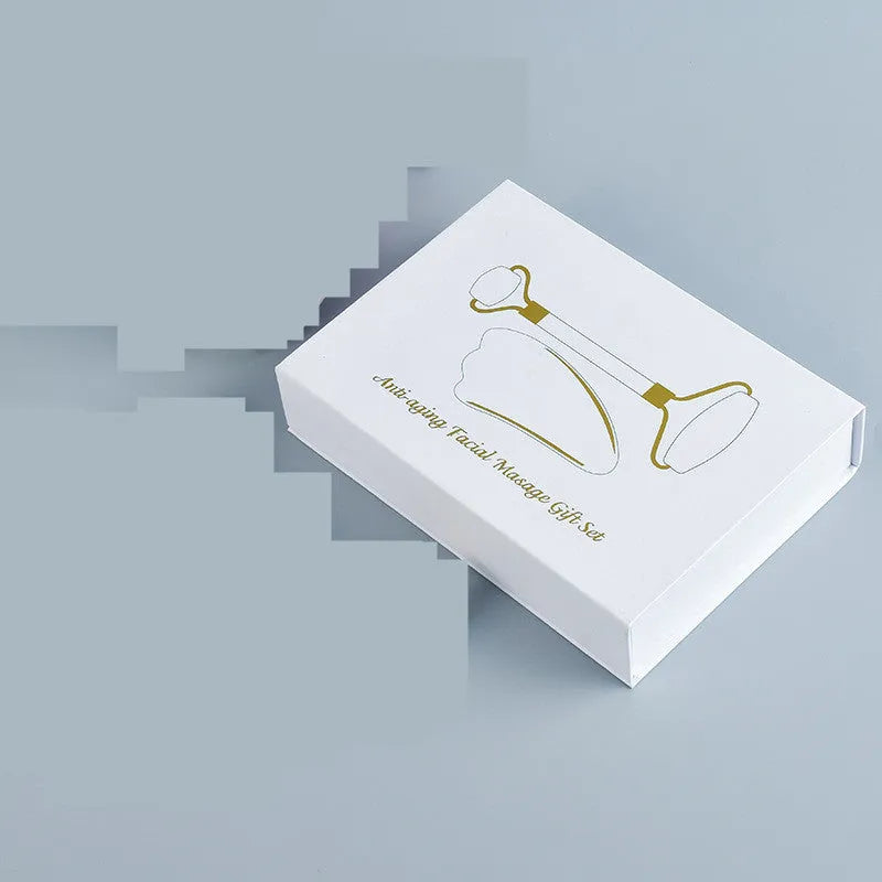 White jade double-headed facial roller and gua sha scraping board set on a neutral background.
