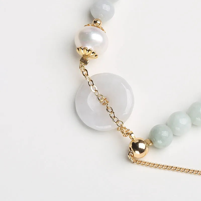 Close-up of a women's pearl bracelet with a natural emerald peace buckle charm and a jade round pendant.