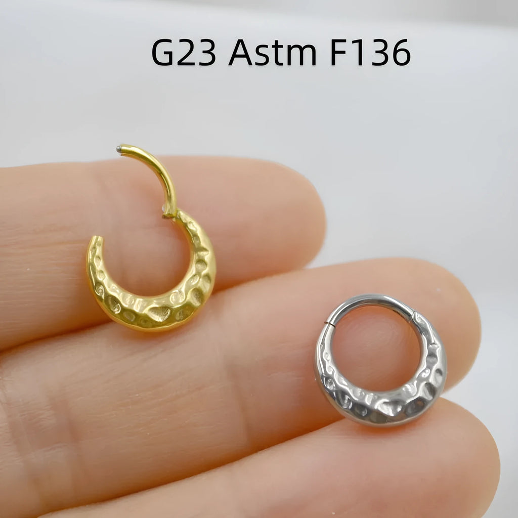 Close-up of a carved concave-convex titanium nose ring in gold finish, showing textured surface.