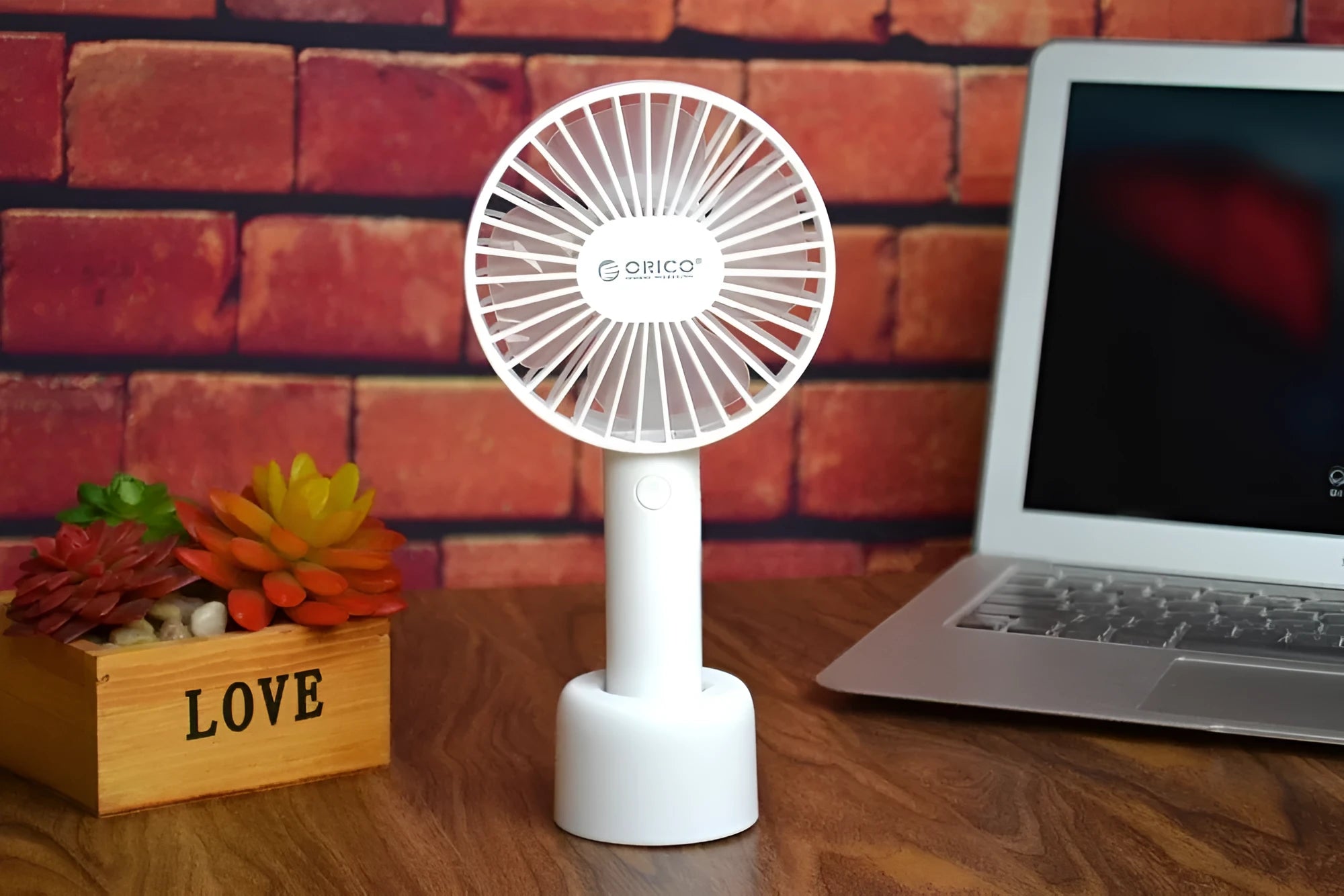 White ORICO FH1 portable USB rechargeable fan on a desk showing its compact size and three-speed button.