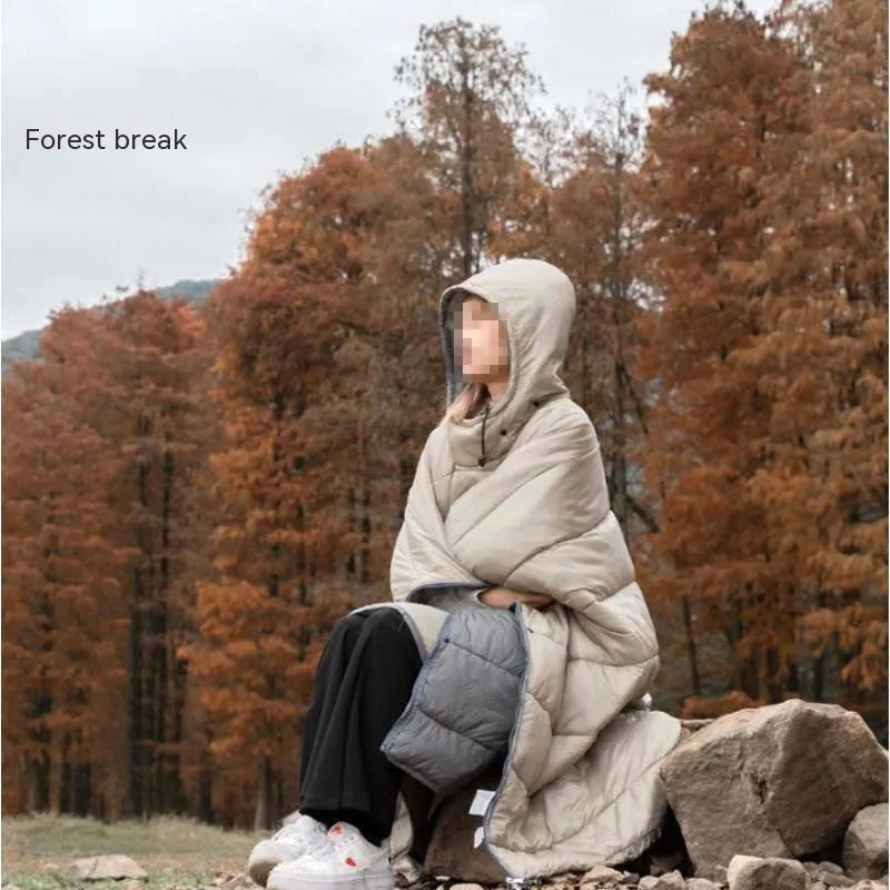 Adult wearing grey nylon cloak sleeping bag as wearable camping blanket outdoors