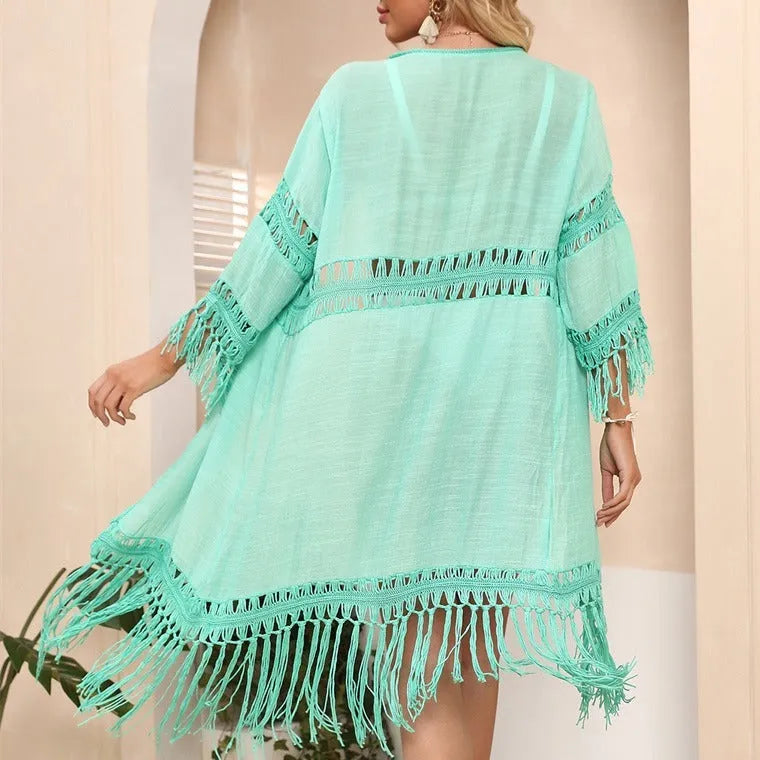 Women's yellow hand-crocheted beach cover-up cardigan with tassel trim on a hanger.