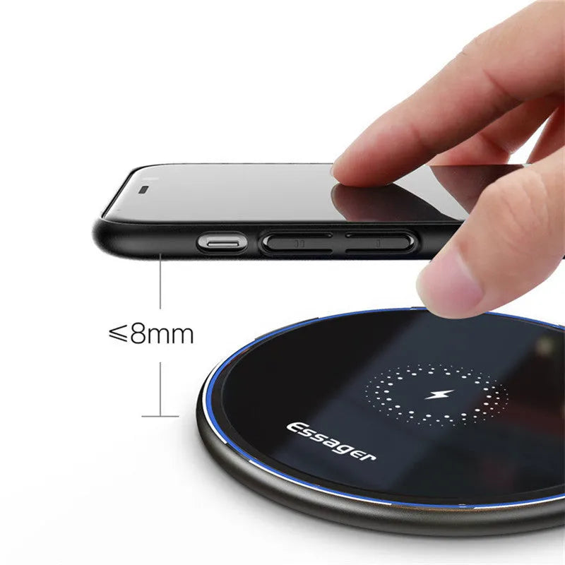 Black wireless charging pad on desk with phone charging, showing blue LED indicator light