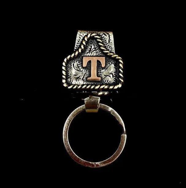 Handmade metal keychain shaped like a cow tag with a belt-style link for keys.
