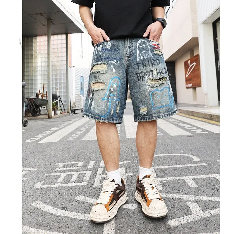 Blue men's denim shorts with ripped knees and graffiti图案, featuring a straight leg and zipper fly.