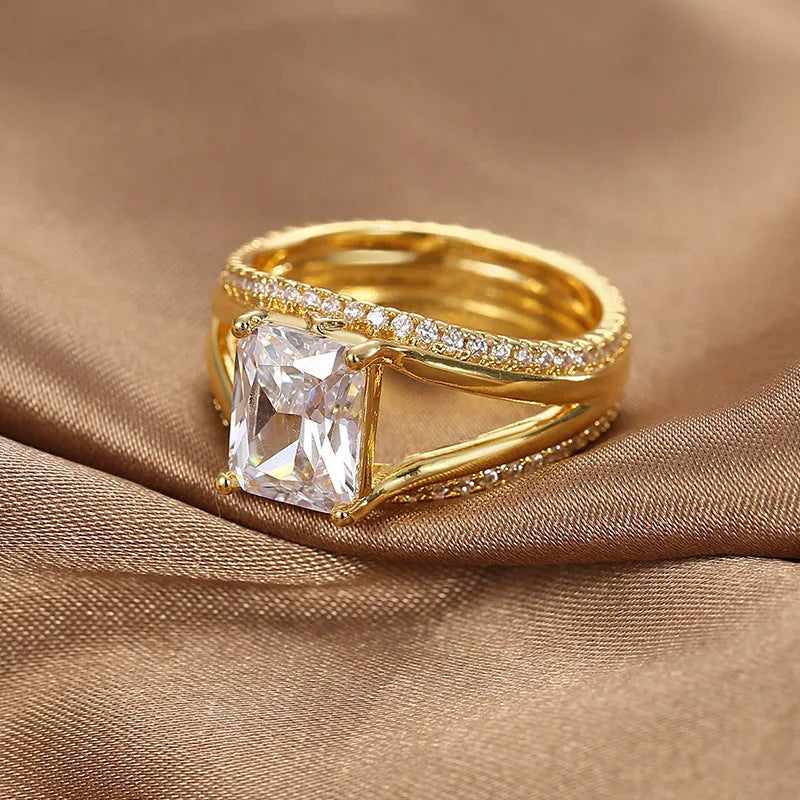 Gold-coloured geometric women's ring with a square zircon stone, shown on a finger.