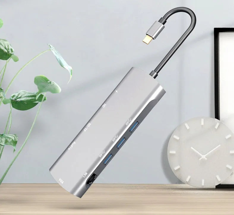 Grey aluminium USB-C docking station showing HDMI, VGA, USB 3.0, and USB-C PD ports with a short attached cable.
