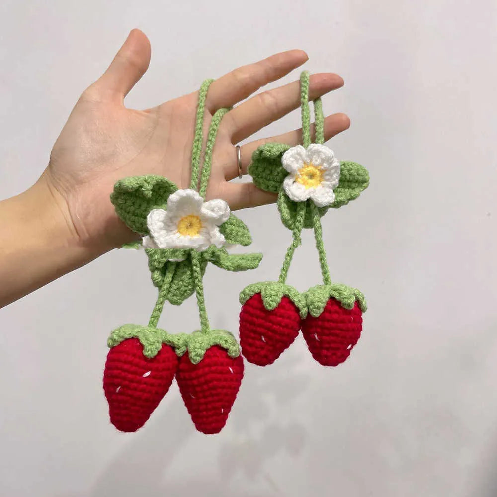 Handwoven strawberry-shaped car pendant made from cotton and hemp fibres on a grey background.