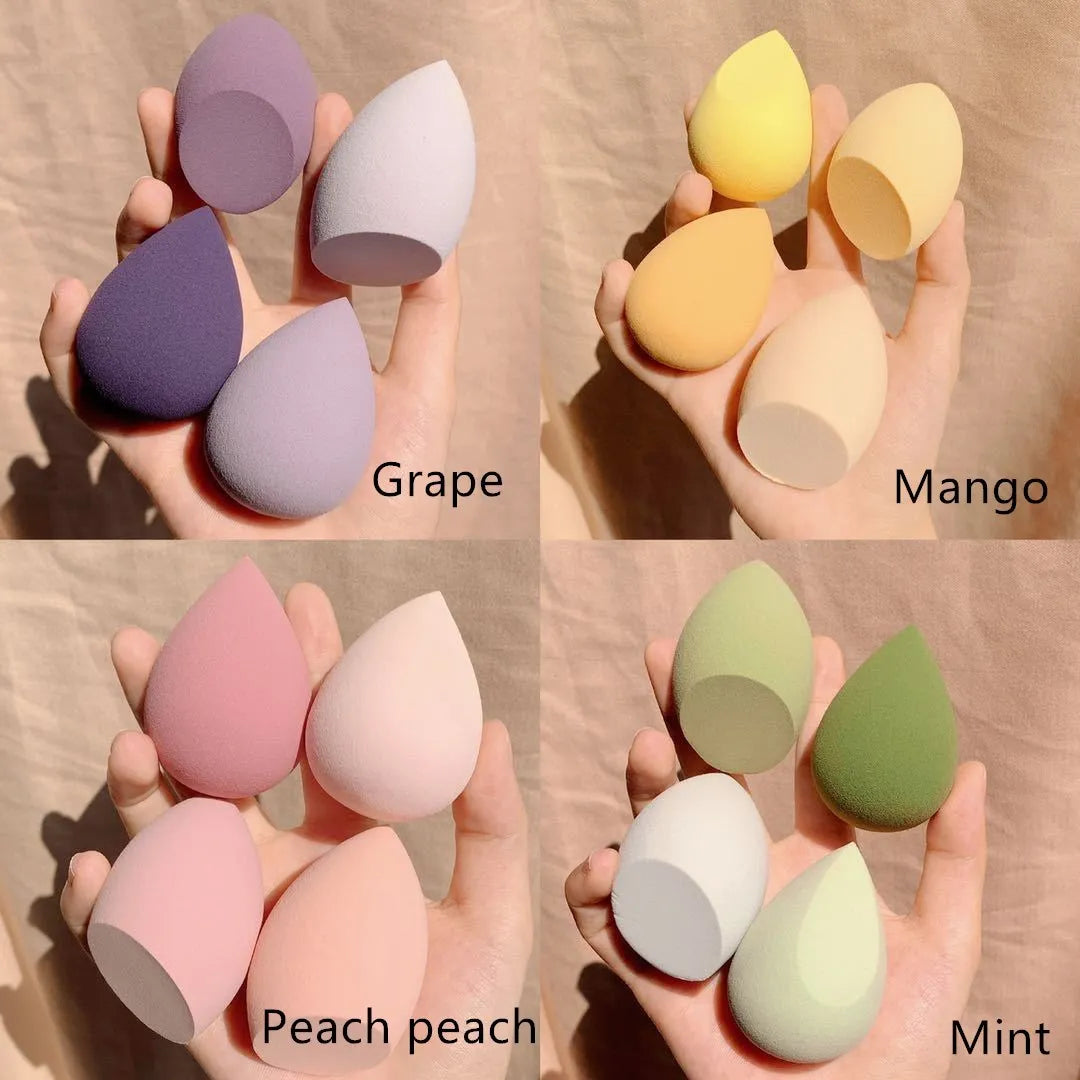 Set of four colourful synthetic makeup beauty egg sponges in grape, mango, mint, and peach, each roughly 6cm cubed.