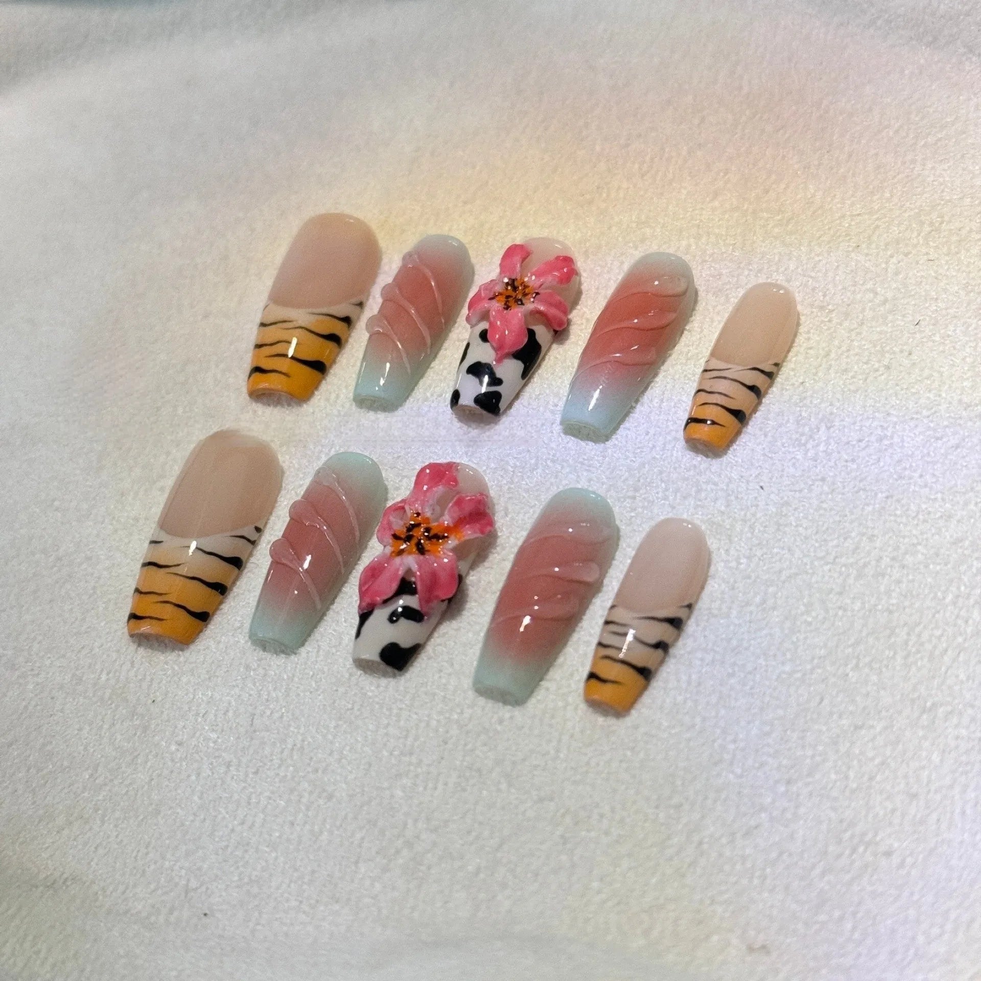 Close-up of zebra pattern artificial nails with embossed lily flower and leopard print designs, shown in long wear-resistant style.
