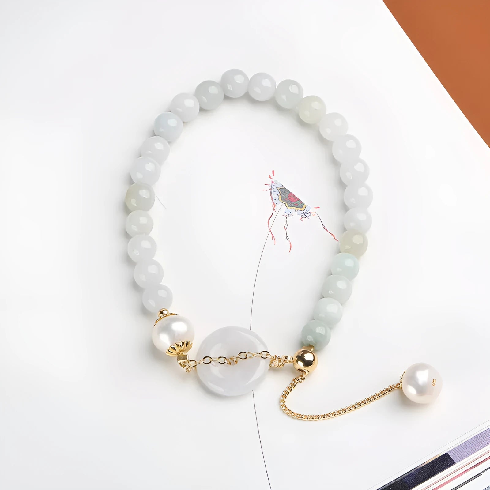 Close-up of a women's pearl bracelet with a natural emerald peace buckle charm and a jade round pendant.
