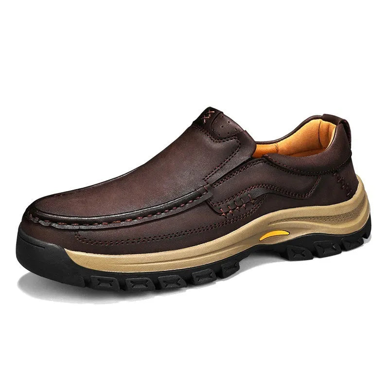 Men's black leather mountaineering shoes with thick rubber soles and round toe on a rocky path.
