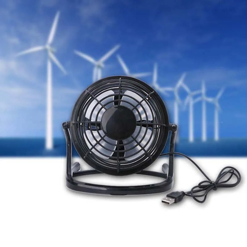 Small black USB desk fan with adjustable angle on wooden desk next to laptop