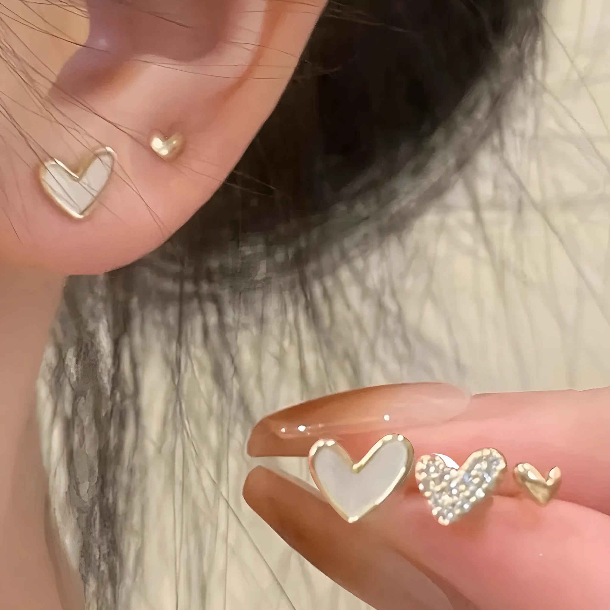 Three pairs of heart-shaped alloy earrings in gold, black, black and white, and pink colours on a white background.