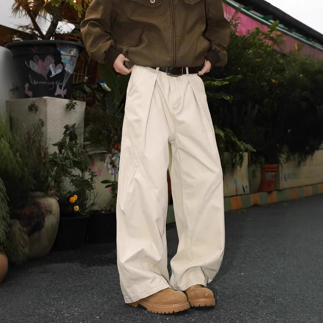 Man wearing straight-leg pleated trousers in a cotton-polyester blend, available in black, brown, and apricot.