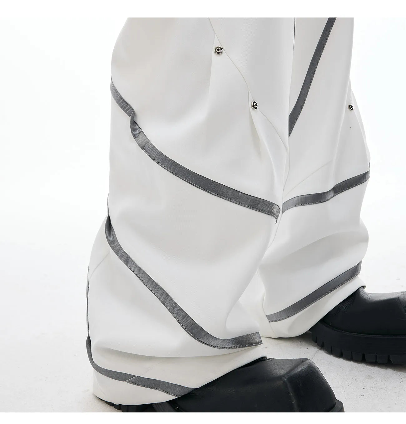 Men's black trousers with three-dimensional cutting and metal rivet pleats on a white background.