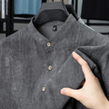Men's loose grey linen shirt with stand collar, cardigan style, on a hanger.