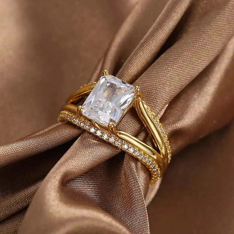 Gold-coloured geometric women's ring with a square zircon stone, shown on a finger.