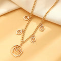Gold spiral donut necklace, bracelet, and earrings set for women on a grey background.