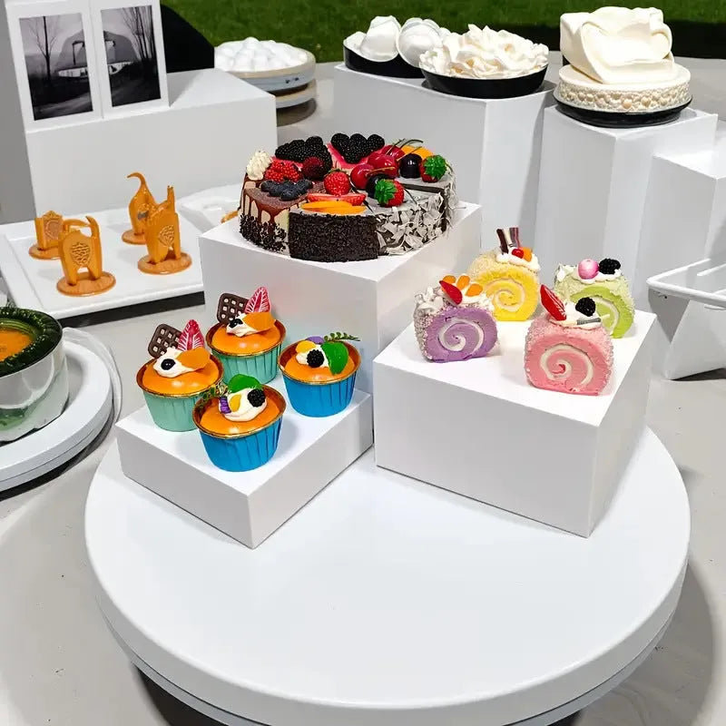 Set of six white plastic cube dessert display stands arranged on a table.