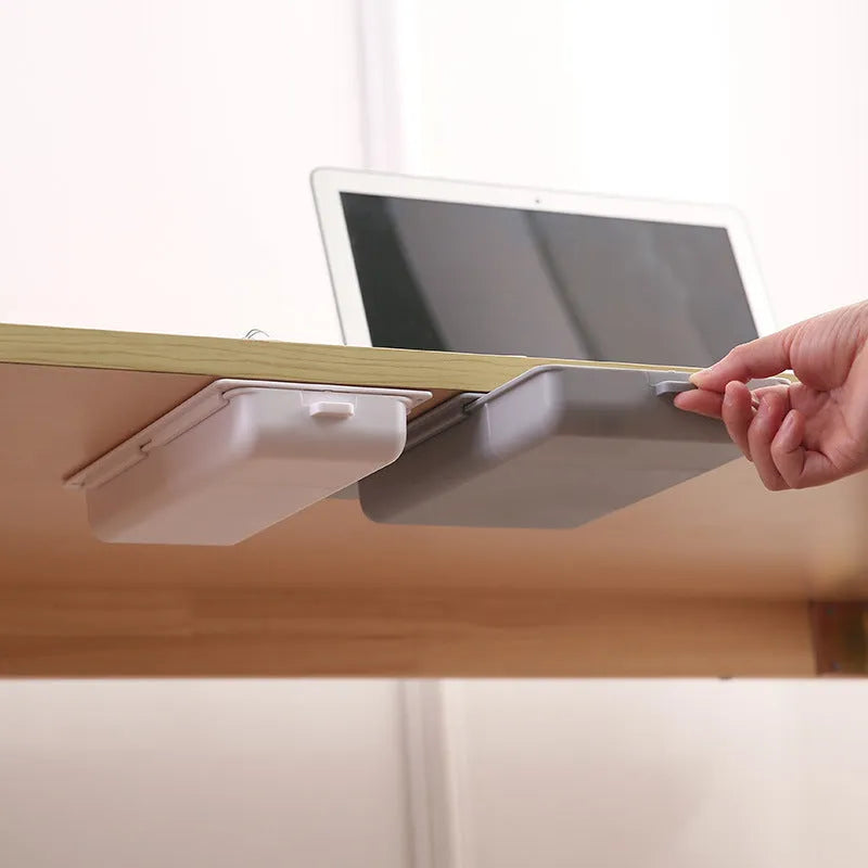 Small grey plastic drawer with a white cover and internal grid, shown mounted under a wooden table.