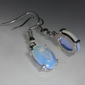 Pair of pale opal-colour drop earrings with a small cross detail on an elliptical alloy pendant.