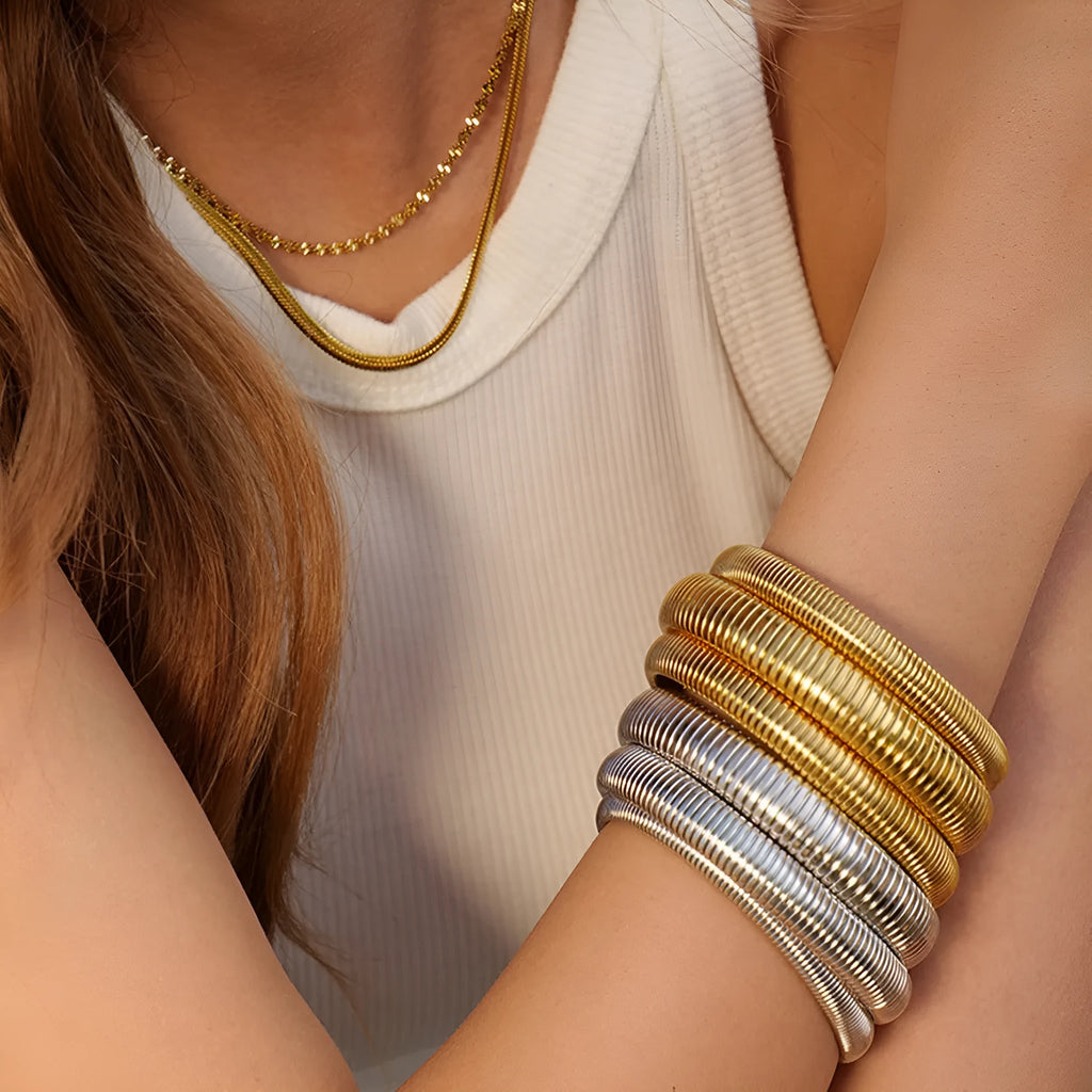 Gold titanium steel bracelet with wide vertical stripe ring pattern and elastic band on a wrist.