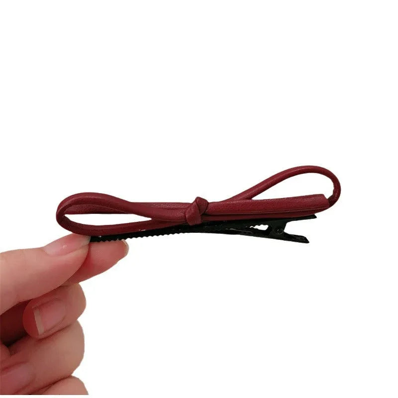Close-up of a wine red leather bow-shaped barrette hair clip on a dark background.