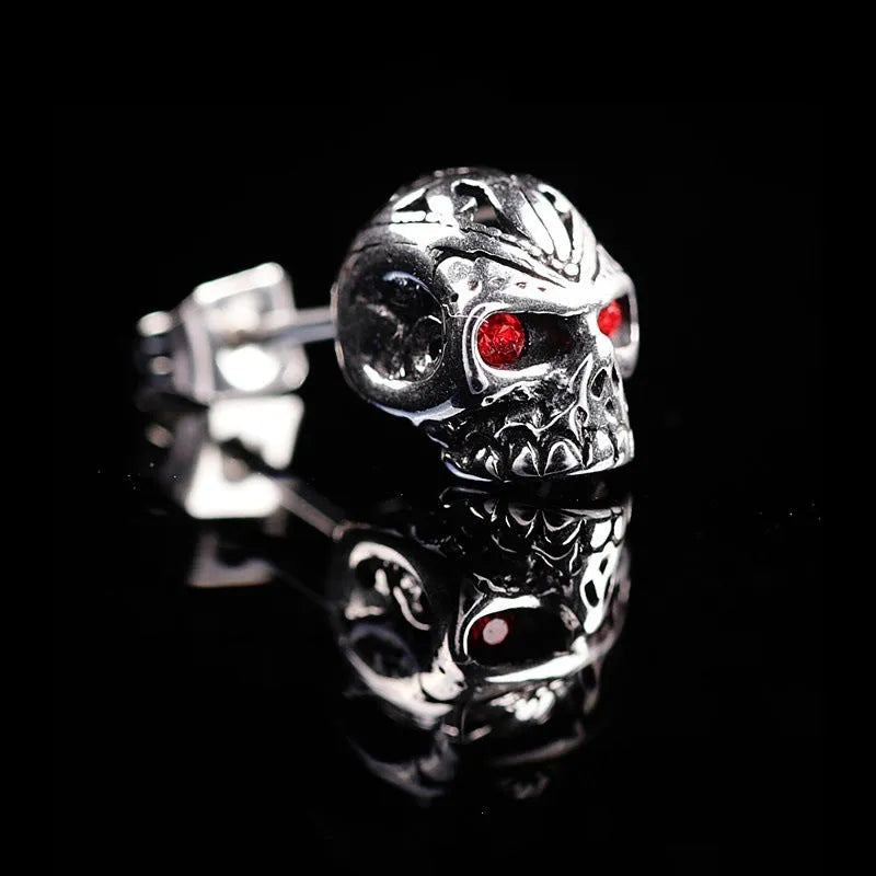 Pair of red eye skull stud earrings with alloy and gemstone inlay on a white background.