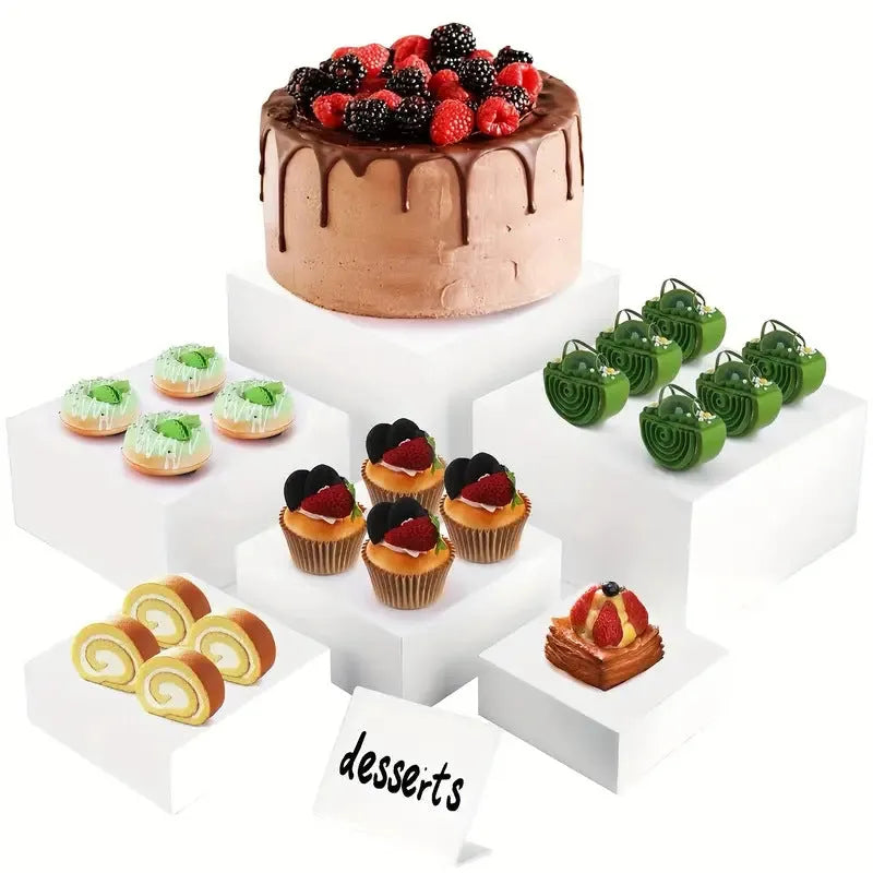 Set of six white plastic cube dessert display stands arranged on a table.