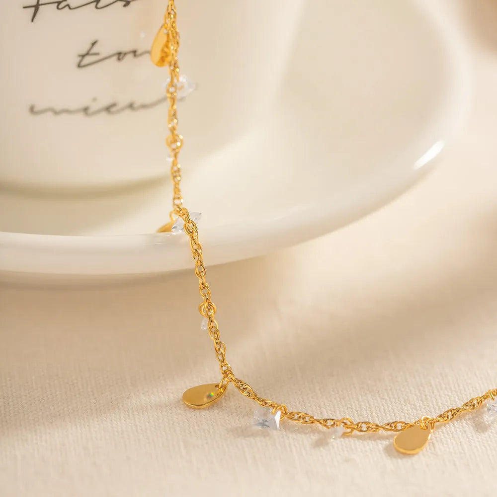 Close-up of a women's stainless steel anklet with a geometric water drop tassel charm on an adjustable chain.