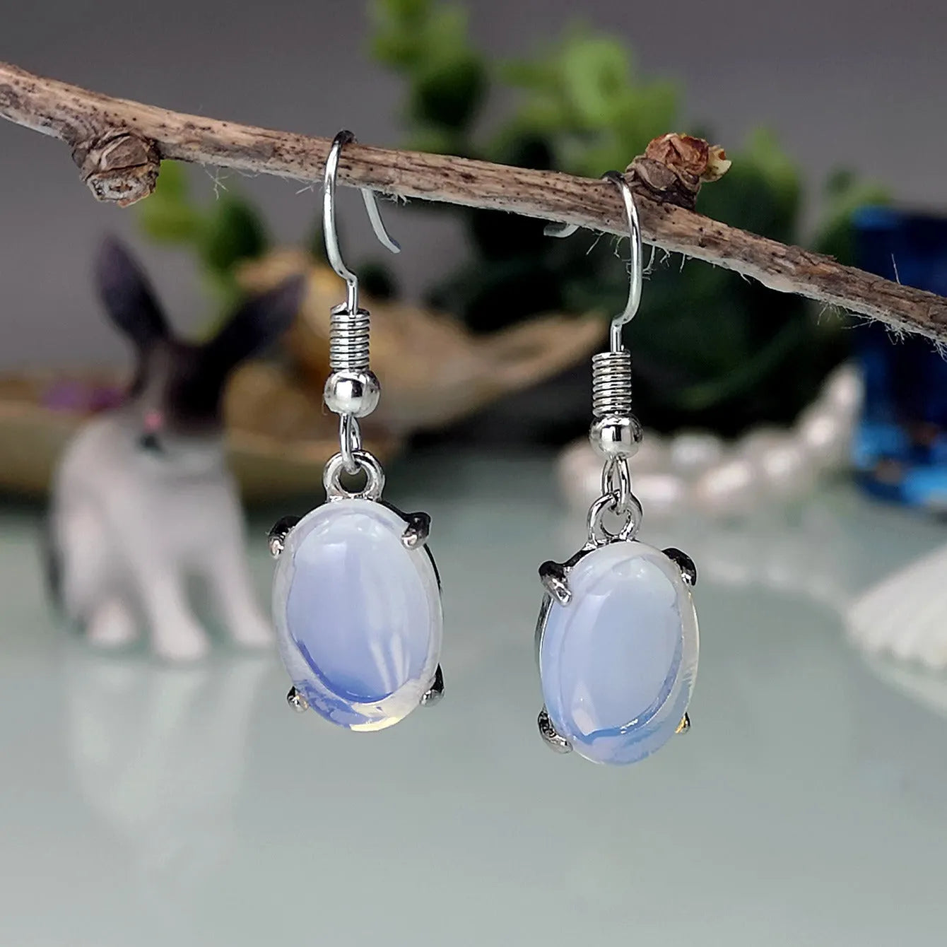 Pair of pale opal-colour drop earrings with a small cross detail on an elliptical alloy pendant.