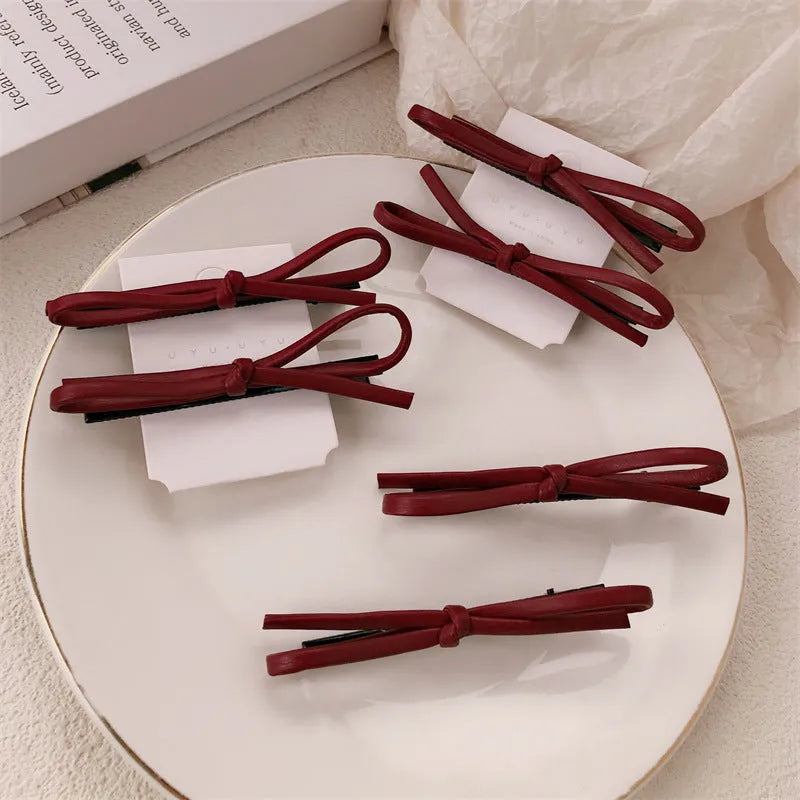 Close-up of a wine red leather bow-shaped barrette hair clip on a dark background.