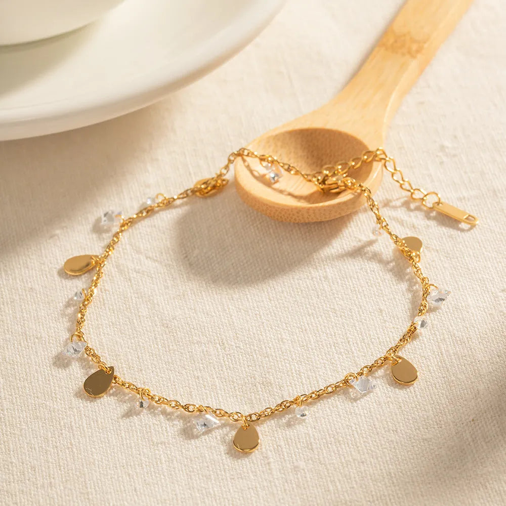 Close-up of a women's stainless steel anklet with a geometric water drop tassel charm on an adjustable chain.