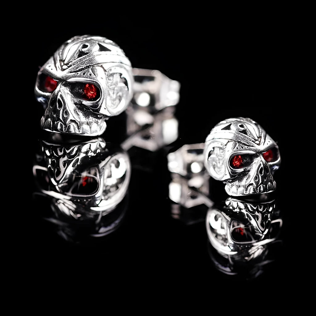 Pair of red eye skull stud earrings with alloy and gemstone inlay on a white background.