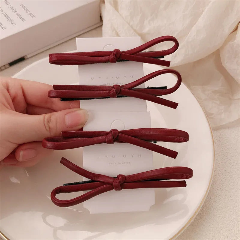Close-up of a wine red leather bow-shaped barrette hair clip on a dark background.