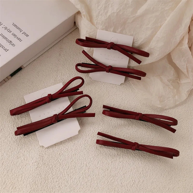 Close-up of a wine red leather bow-shaped barrette hair clip on a dark background.