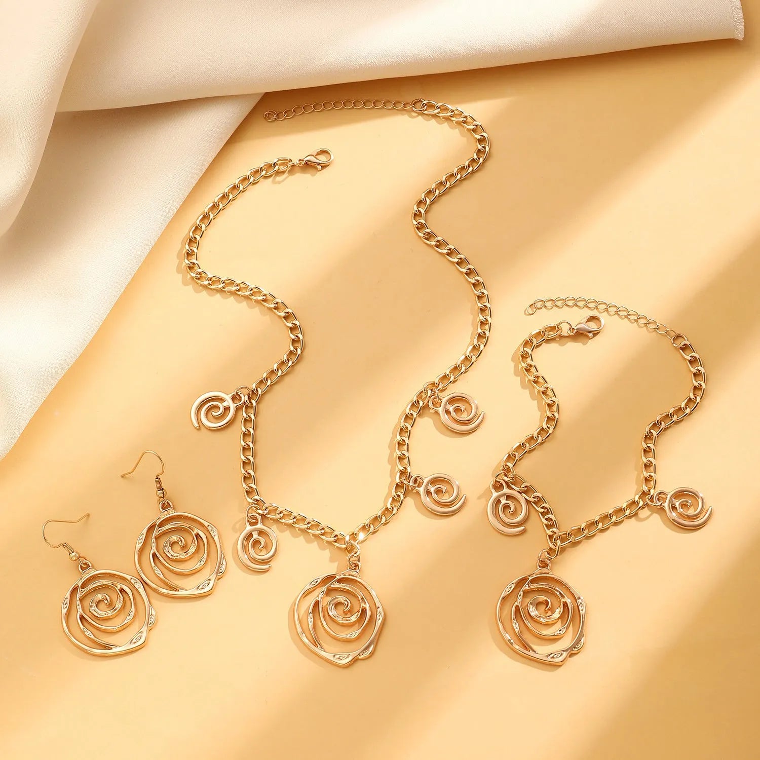 Gold spiral donut necklace, bracelet, and earrings set for women on a grey background.
