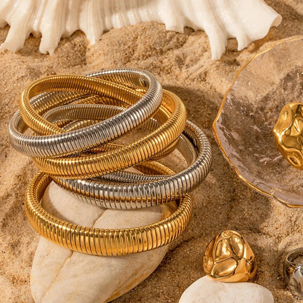 Gold titanium steel bracelet with wide vertical stripe ring pattern and elastic band on a wrist.