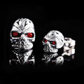 Pair of red eye skull stud earrings with alloy and gemstone inlay on a white background.