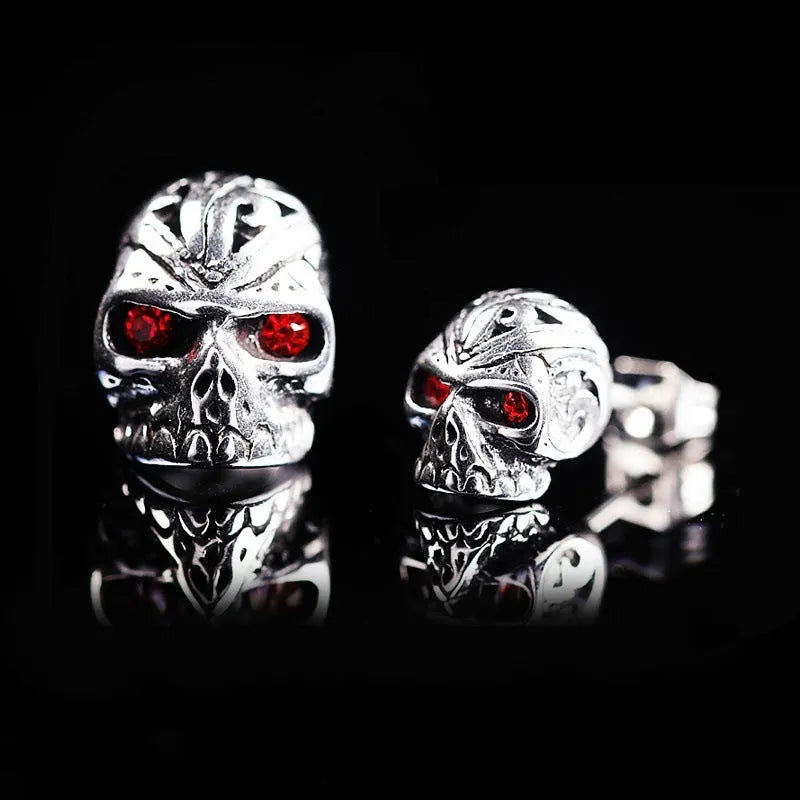 Pair of red eye skull stud earrings with alloy and gemstone inlay on a white background.