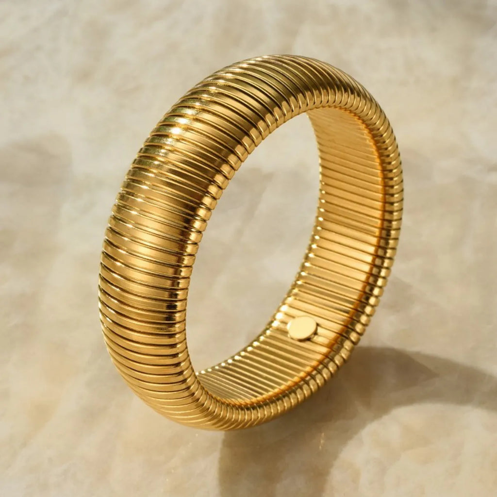 Gold titanium steel bracelet with wide vertical stripe ring pattern and elastic band on a wrist.